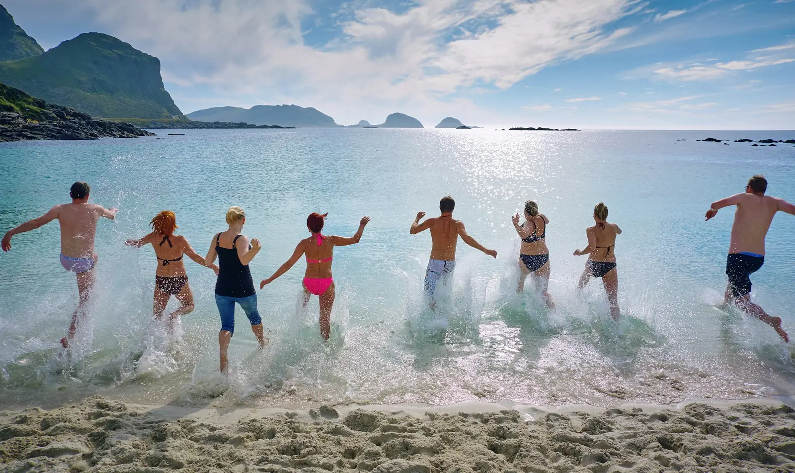 Group of friends running into the sea on a sunny beach