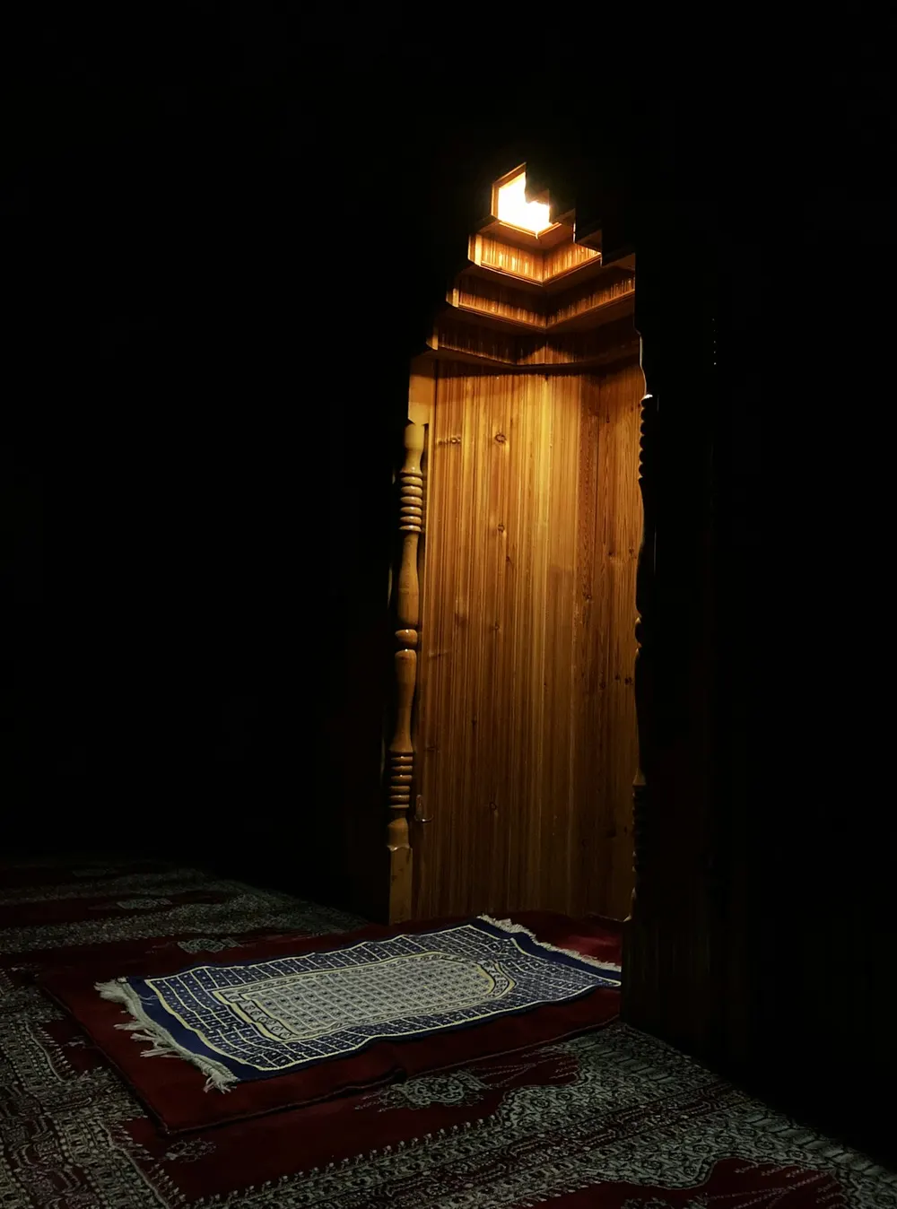 Prayer rug laid in front of a wooden mihrab