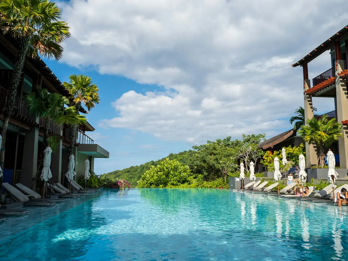 Quiet resort pool surrounded by palm trees and green hills in Thailand